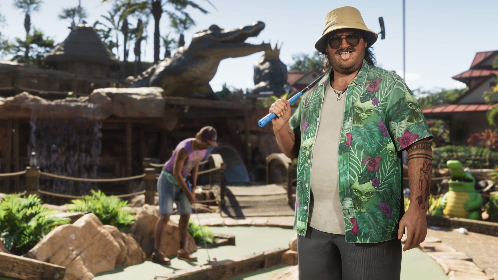 Cal Hampton in Blumenhemd und Fischerhut hält einen Golfschläger auf einer Minigolfanlage mit riesiger Alligatorfigur