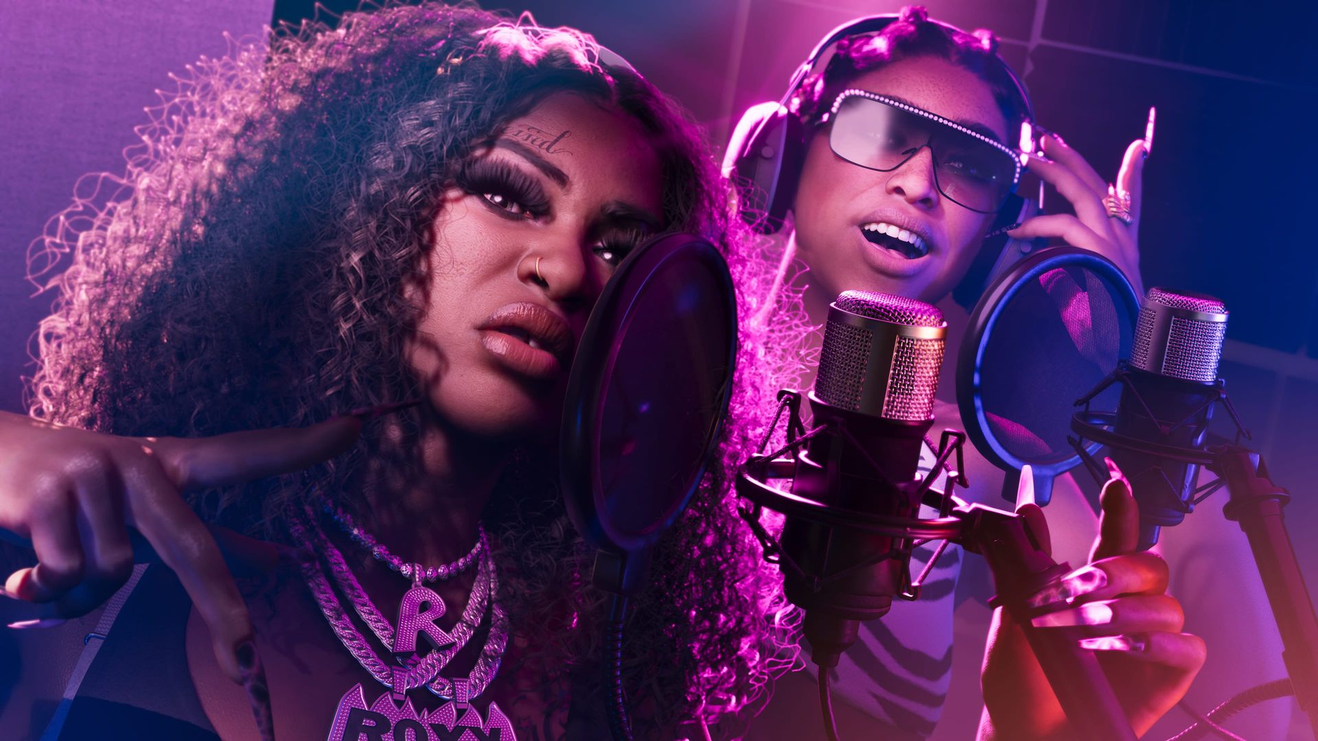 Die beiden Mitglieder von Real Dimez singen in pinkem Licht in ein Studiomikrofon